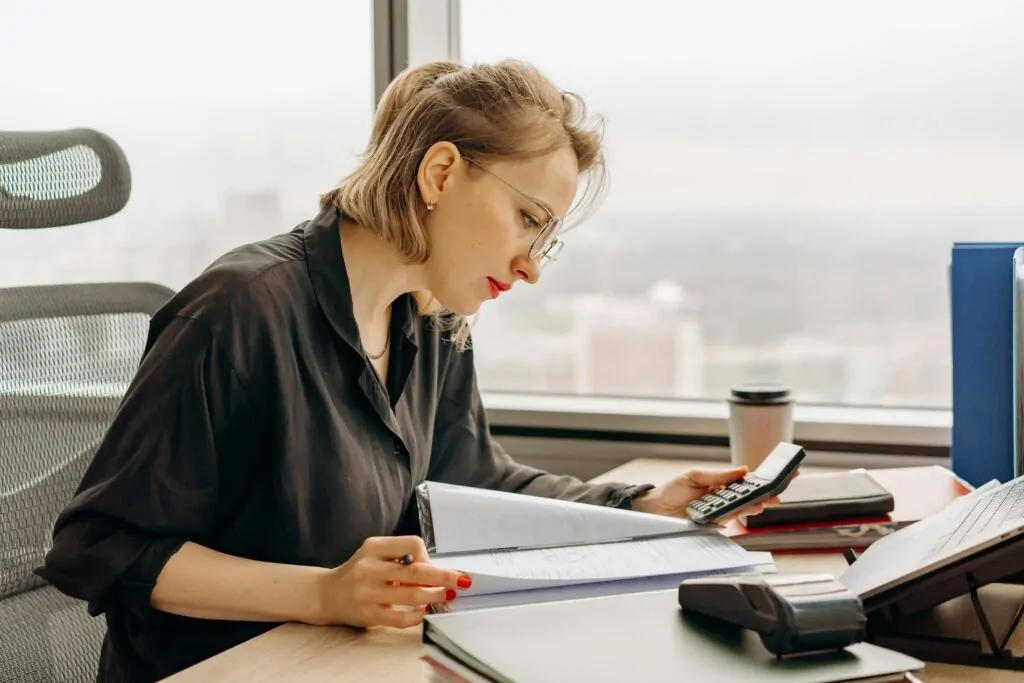 Femme travaille avec documents et calculatrice au bureau.